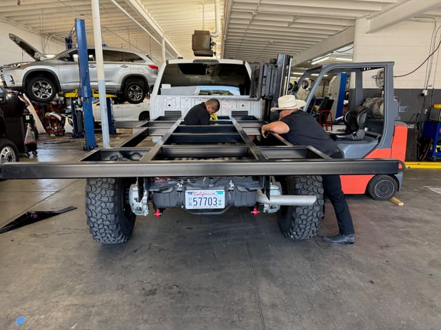 Sub-frame being lowered onto the F-550 frame rails inside the shop